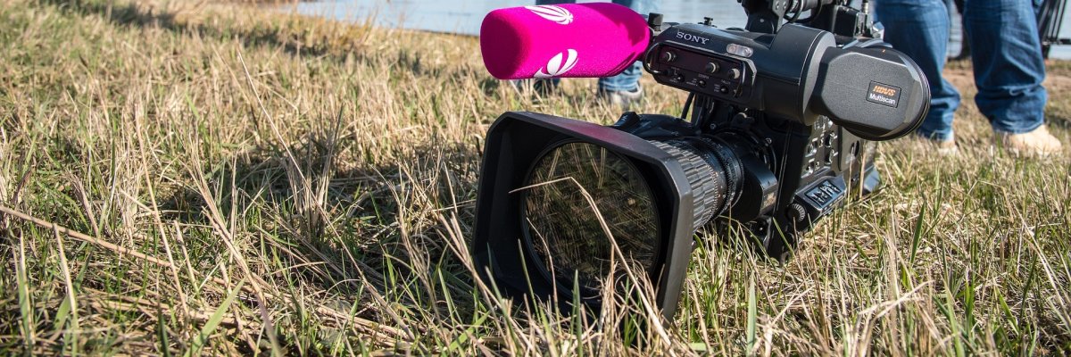 Fernsehkamera liegt im Gras, im Hintergrund zwei Personen