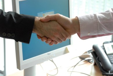 Symbolisches Händeschütteln vor einem Computerbildschirm