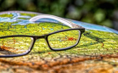 Eine schwarze Lesebrille liegt aufgeklappt auf einer farbigen Landkarte.