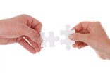 zwei Hände führen jeweils ein weißes Puzzleteil zusammen als Zeichen der Zusammenarbeit