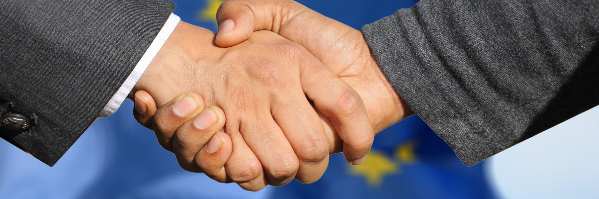 Handschlag mit EU-Flagge im Hintergrund