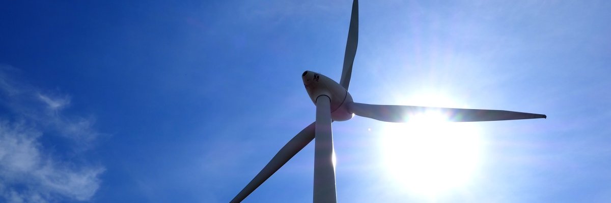 Ein Windkraftrad vor blauem Himmel, hinter einem Rotorblatt scheint die Sonne hervor